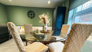 Un coin repas avec une table en verre entourée de chaises à motifs, une horloge au mur et une fenêtre donnant sur des immeubles.