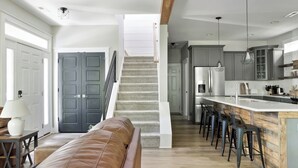 Una cocina moderna con una isla central, taburetes de bar y una escalera que sube a otro nivel.
