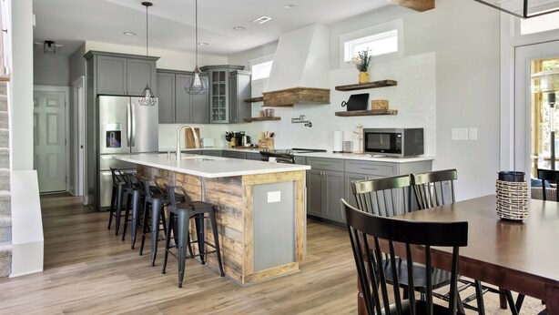 Una cocina moderna con una isla central, taburetes de bar y una mesa de comedor con sillas.