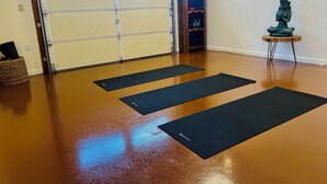 A room with a wooden floor, a closed garage door, and three black mats arranged for exercise. - Romeo's Roadhouse with Cowboy Pool (Lake Montezuma)