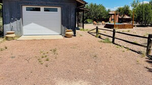 A rustic building with a white garage door, surrounded by a gravel driveway and a wooden fence. - Romeo's Roadhouse with Cowboy Pool (Lake Montezuma)