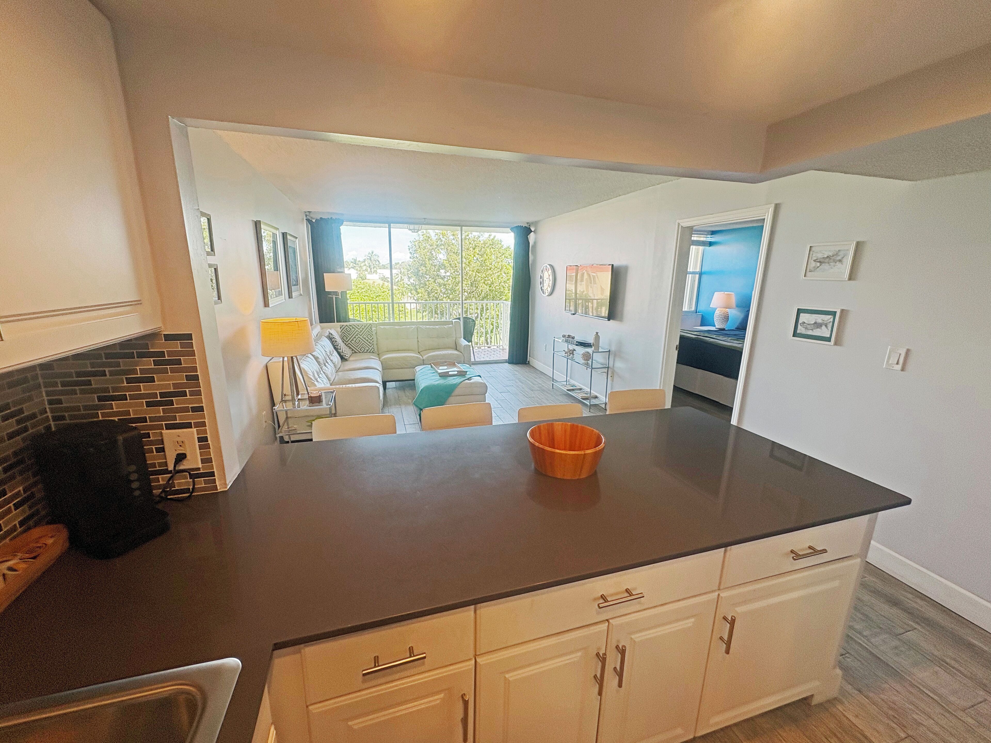 A modern kitchen with a dark countertop, white cabinets, and a dining area with a table and chairs.
