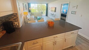 A modern kitchen with a dark countertop, white cabinets, and a dining area with a table and chairs. - Charming Bayside 2 bed, 2 bath Condo at Futura in Islamorada WiFi, Pool, Dockage (Tavernier)