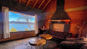 Un intérieur chaleureux avec un sol en pierre, des meubles en bois, une cheminée et une grande fenêtre donnant sur un lac.