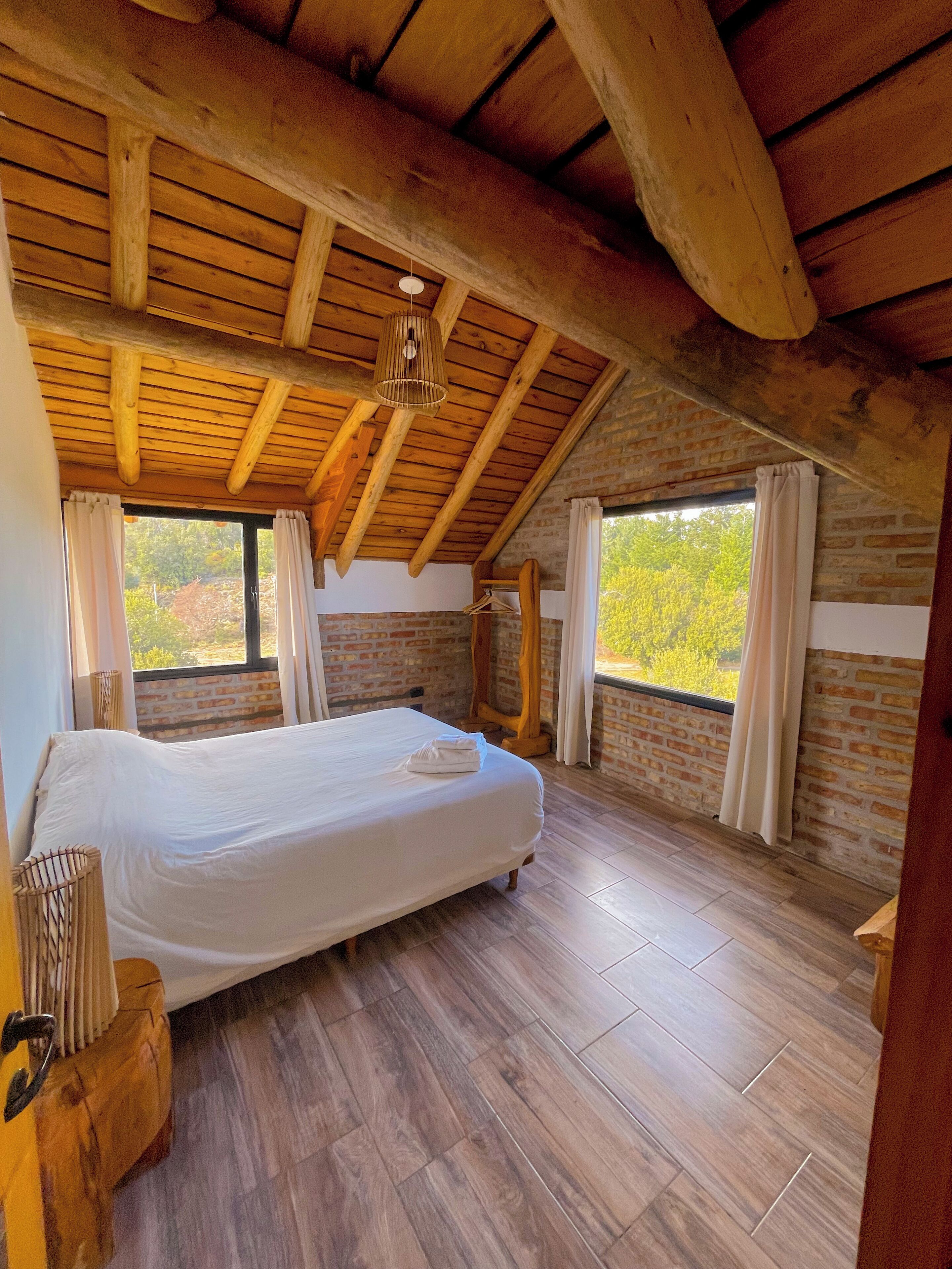 Una camera da letto con soffitto in legno, un letto grande e vista su alberi attraverso una finestra.