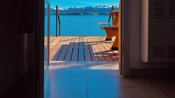 Une terrasse en bois qui mène à un balcon offrant une vue sur un lac et des montagnes.