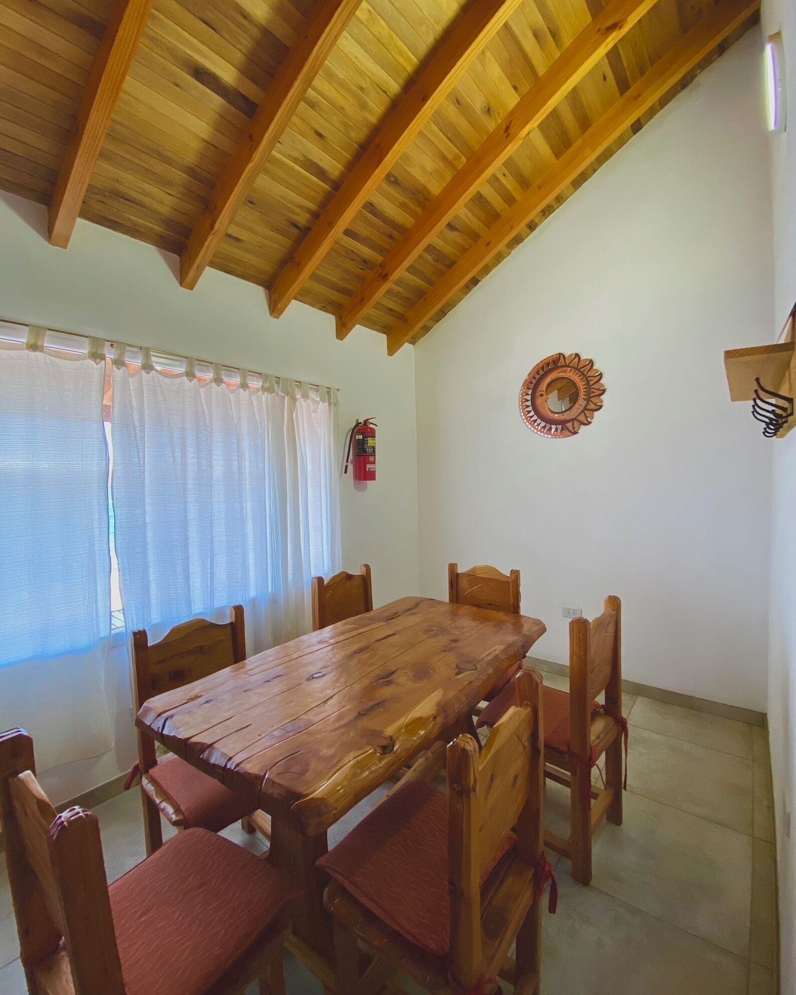 Un coin repas avec une table et des chaises en bois, un extincteur et un miroir décoratif au mur.