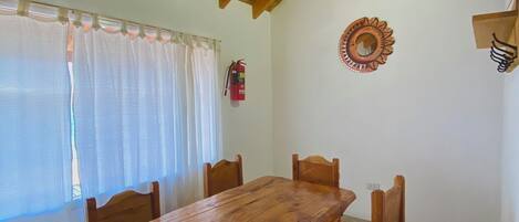 Un coin repas avec une table et des chaises en bois, un extincteur et un miroir décoratif au mur.