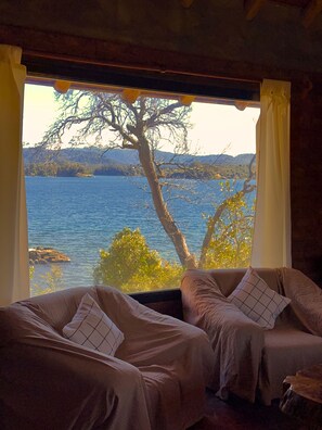 A room with two sofas facing a window overlooking a lake and trees. - Complejo Don Cirilo (Villa Pehuenia)