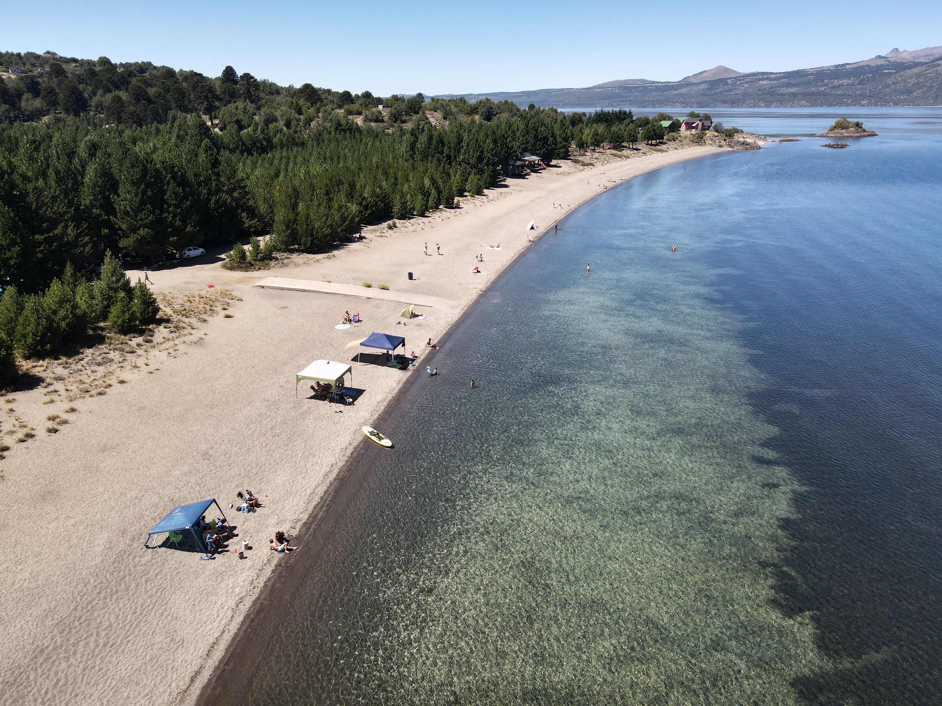 Une plage à l’eau claire, avec des tentes et une zone boisée.