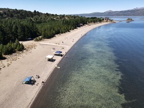 A beach with clear water, tents, and a forested area. - Complejo Don Cirilo (Villa Pehuenia)