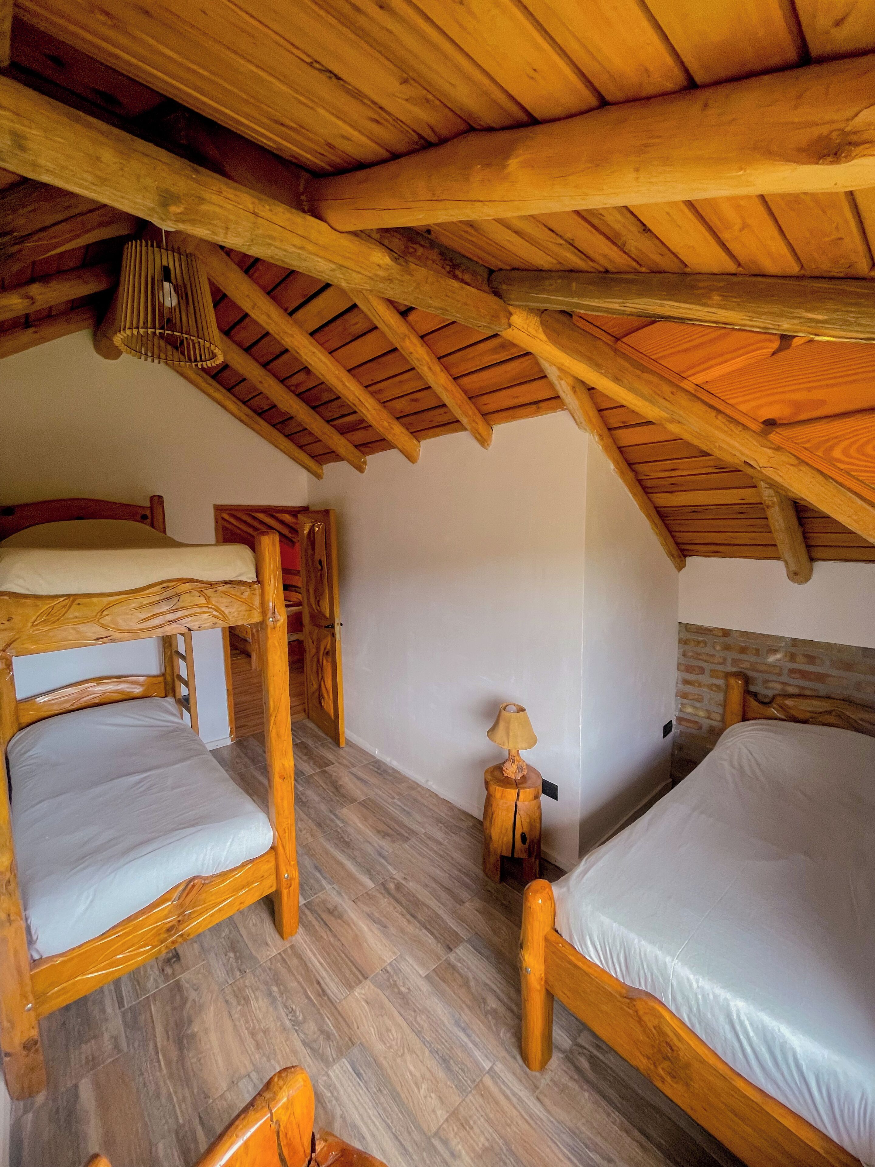 Quarto com beliche de madeira, teto inclinado e uma pequena mesa com abajur.