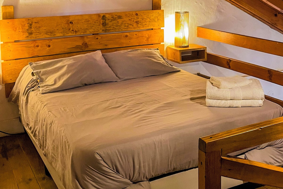 A bedroom with a wooden headboard, a bed with white linens, and a nightstand with a lamp.
