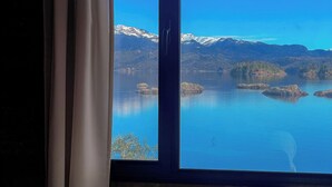 Une chambre d’hôtel avec un lit, une fenêtre donnant sur un lac et des montagnes, et une pile d’serviettes sur le lit.