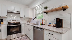 A modern kitchen with white cabinets, stainless steel appliances, a dishwasher, and a coffee maker. - Updated, Cozy home- minutes to Tunnel Vision Trail!  (Bella Vista)