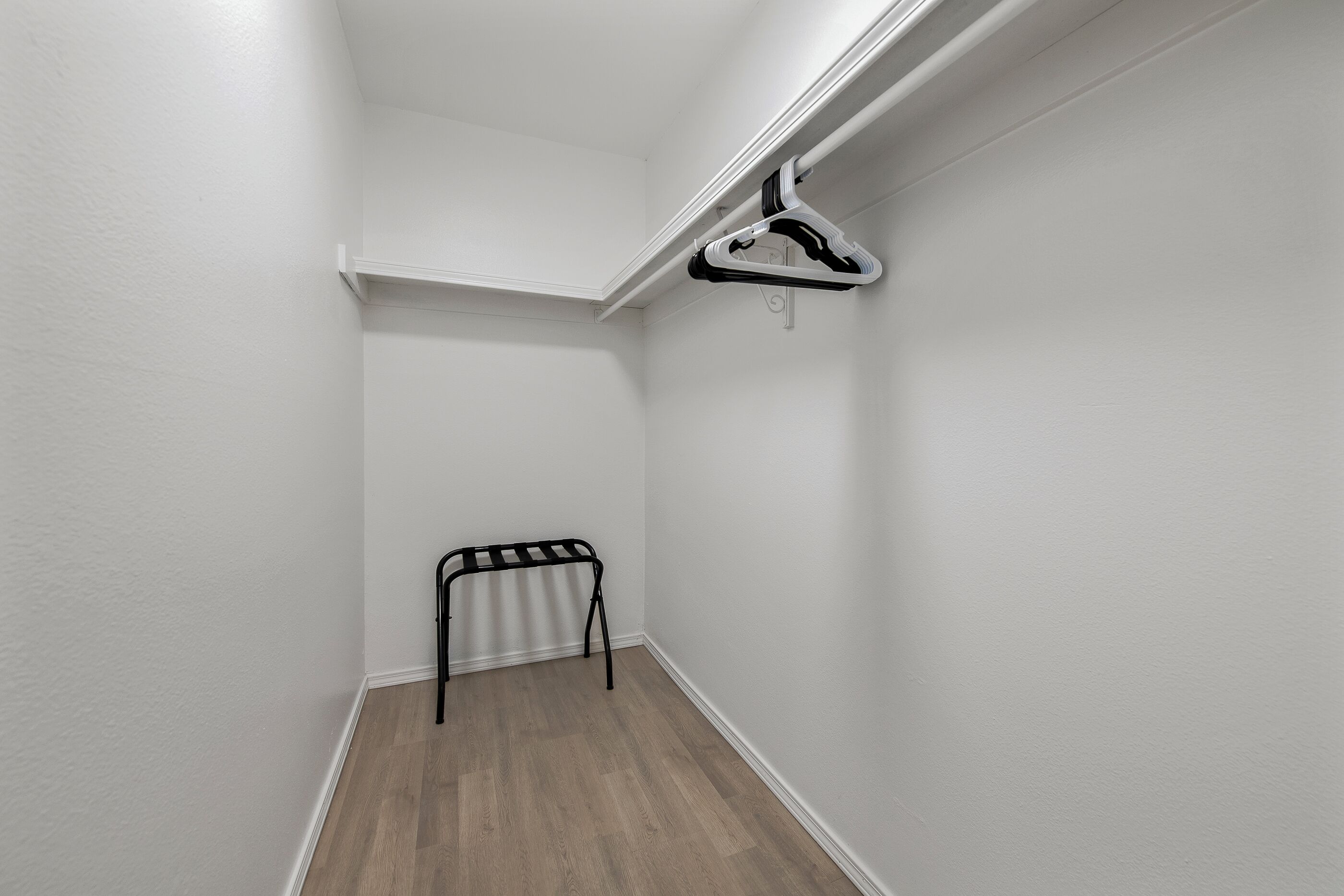 Une petite pièce vide aux murs blancs, avec un plancher en bois, un banc et un portant à vêtements.
