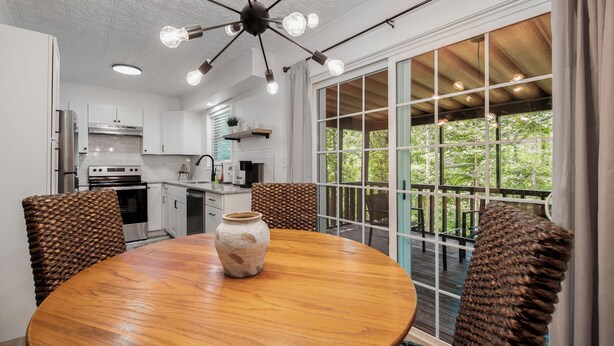 A kitchen with white cabinets, a wooden dining table, and a large window overlooking greenery. - Updated, Cozy home- minutes to Tunnel Vision Trail!  (Bella Vista)