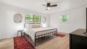 A bedroom with a bed, a ceiling fan, two windows with blinds, a round mirror, and a red rug. - Updated, Cozy home- minutes to Tunnel Vision Trail!  (Bella Vista)
