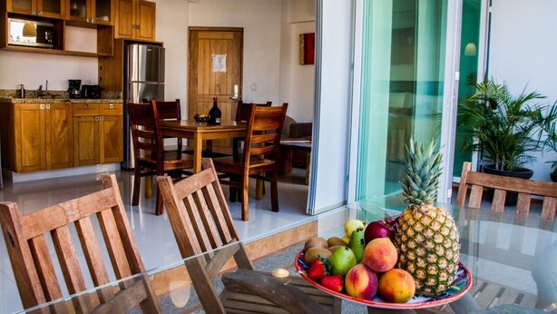 A modern kitchen with wooden cabinets, a stainless steel refrigerator, and a dining area with wooden chairs and a glass table. - Andales Suites 101 (Puerto Vallarta)