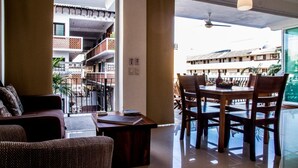 A spacious living area with a balcony, a dining table with chairs, and a view of a building with multiple balconies. - Andales Suites 101 (Puerto Vallarta)