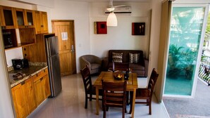 A compact kitchen with wooden cabinets, a refrigerator, and a dining table with chairs. - Andales Suites 101 (Puerto Vallarta)