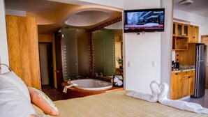 A hotel room with a large bed, a bathroom with a bathtub, a TV mounted on the wall, and wooden cabinets. - Andales Suites 101 (Puerto Vallarta)