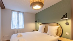 A neatly made bed with white linens, a woven headboard, and two bedside lamps.