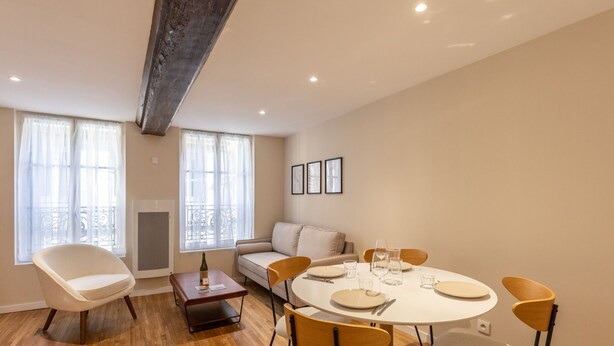 A modern living room with a round dining table set for four, a sofa, and a chair.