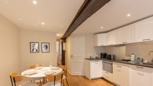 A compact kitchen with white cabinets, a dining table set for four, and a wooden ceiling beam.