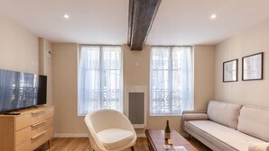 A living room with a TV, a sofa, a chair, and two windows with curtains.