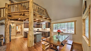 Una cocina amplia con detalles de madera, un comedor con una mesa grande y bancos, y vistas a través de una ventana.