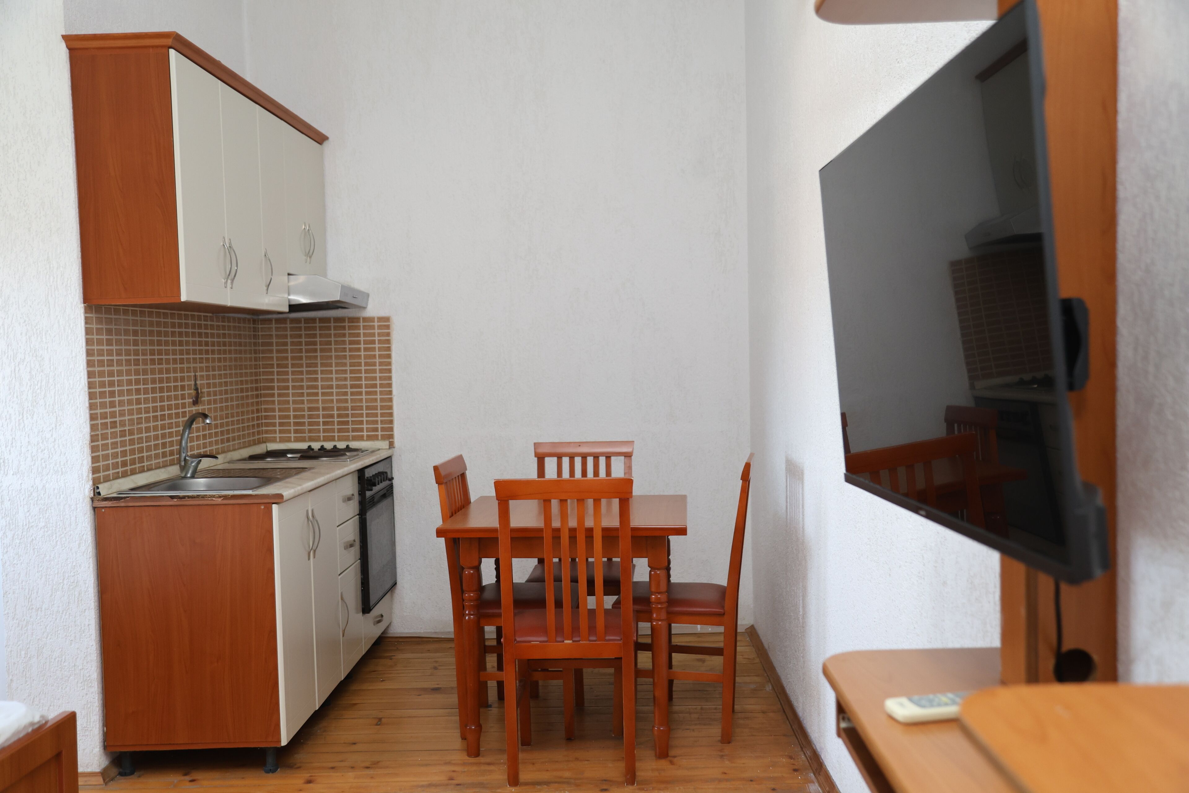 Eine kompakte Küche mit Esstisch und Stühlen, einem Fernseher und einem kleinen Tisch mit Fernbedienung.