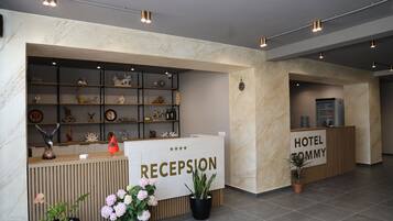A hotel reception area with a reception desk, a display of decorative items, and a sign that reads "HOTEL TOMMY RECEPTION".