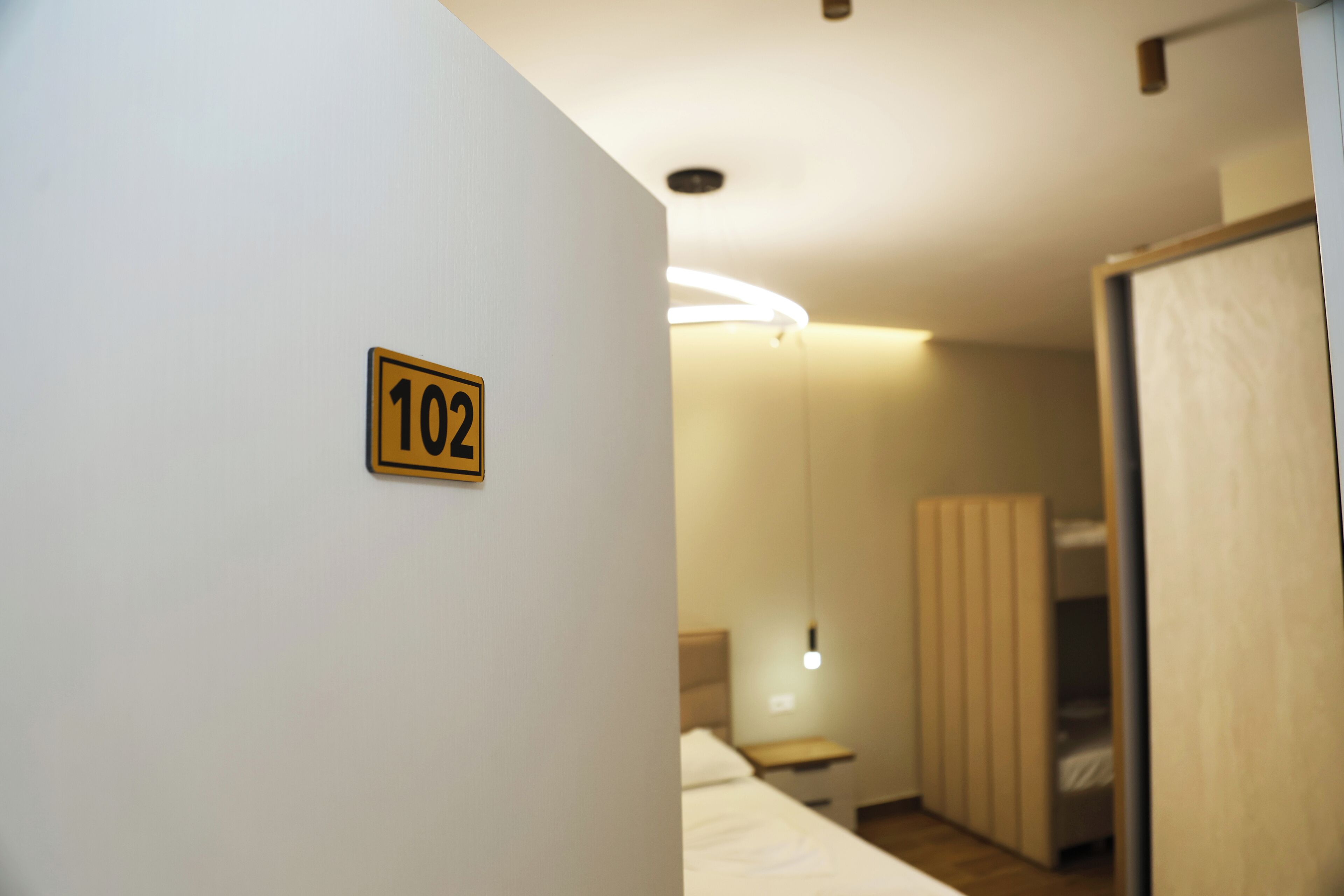 A hotel room with a bed, a bedside table, and a nightstand. There is a sign with the number 102 on the wall.