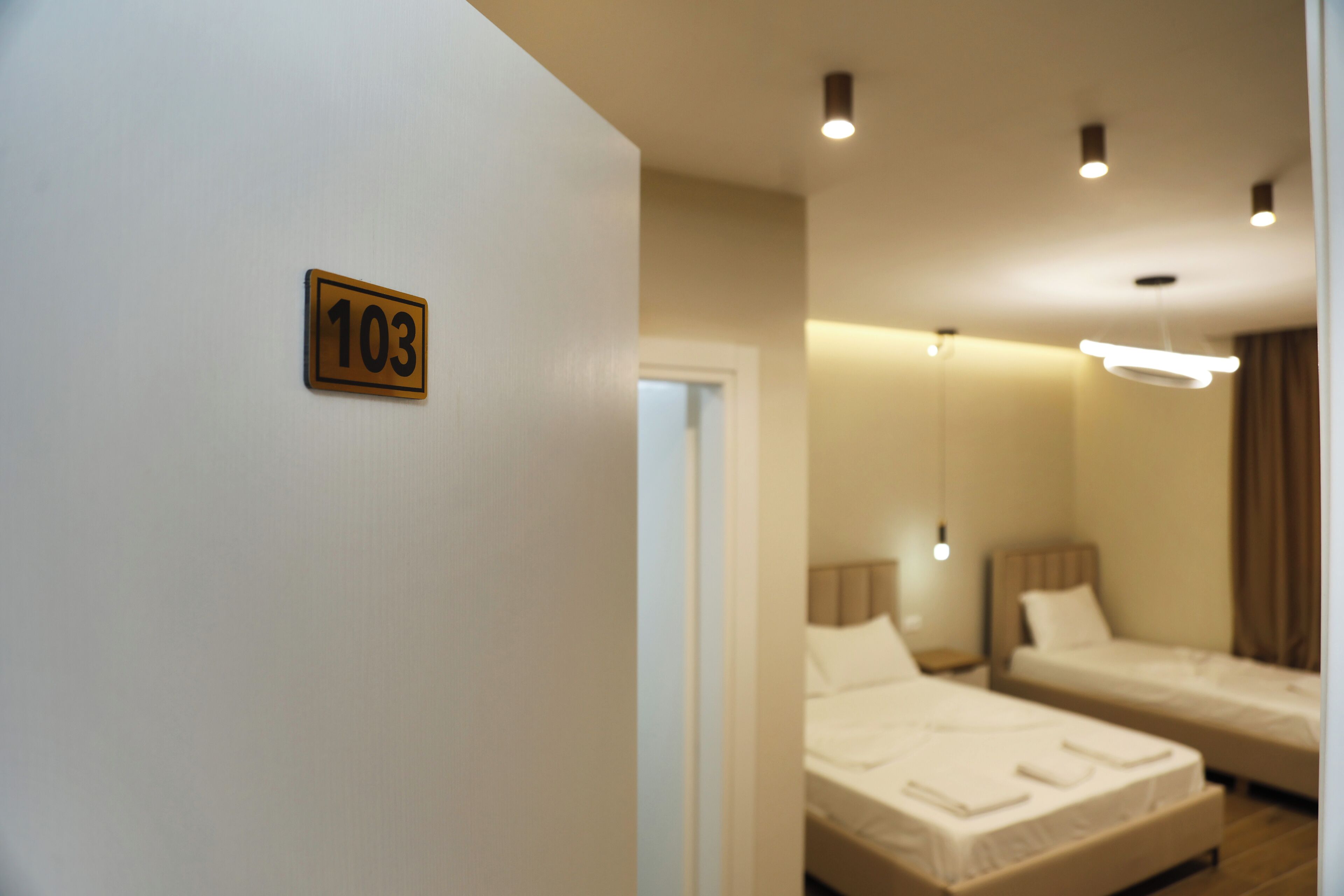 Une chambre d’hôtel avec deux lits, une porte portant un numéro et un luminaire moderne.