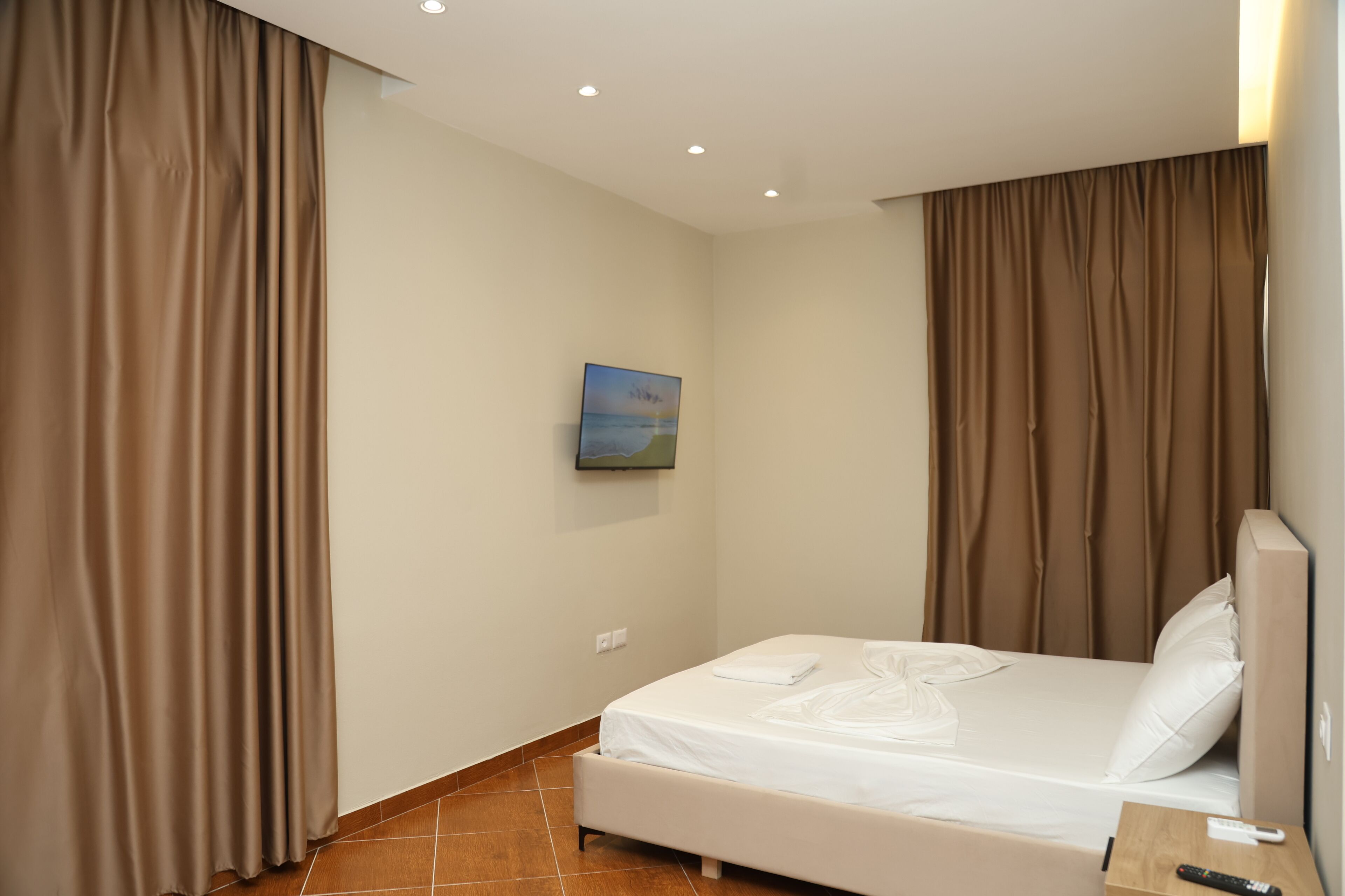 A hotel room with a bed, curtains, a painting on the wall, and a remote control on the nightstand.