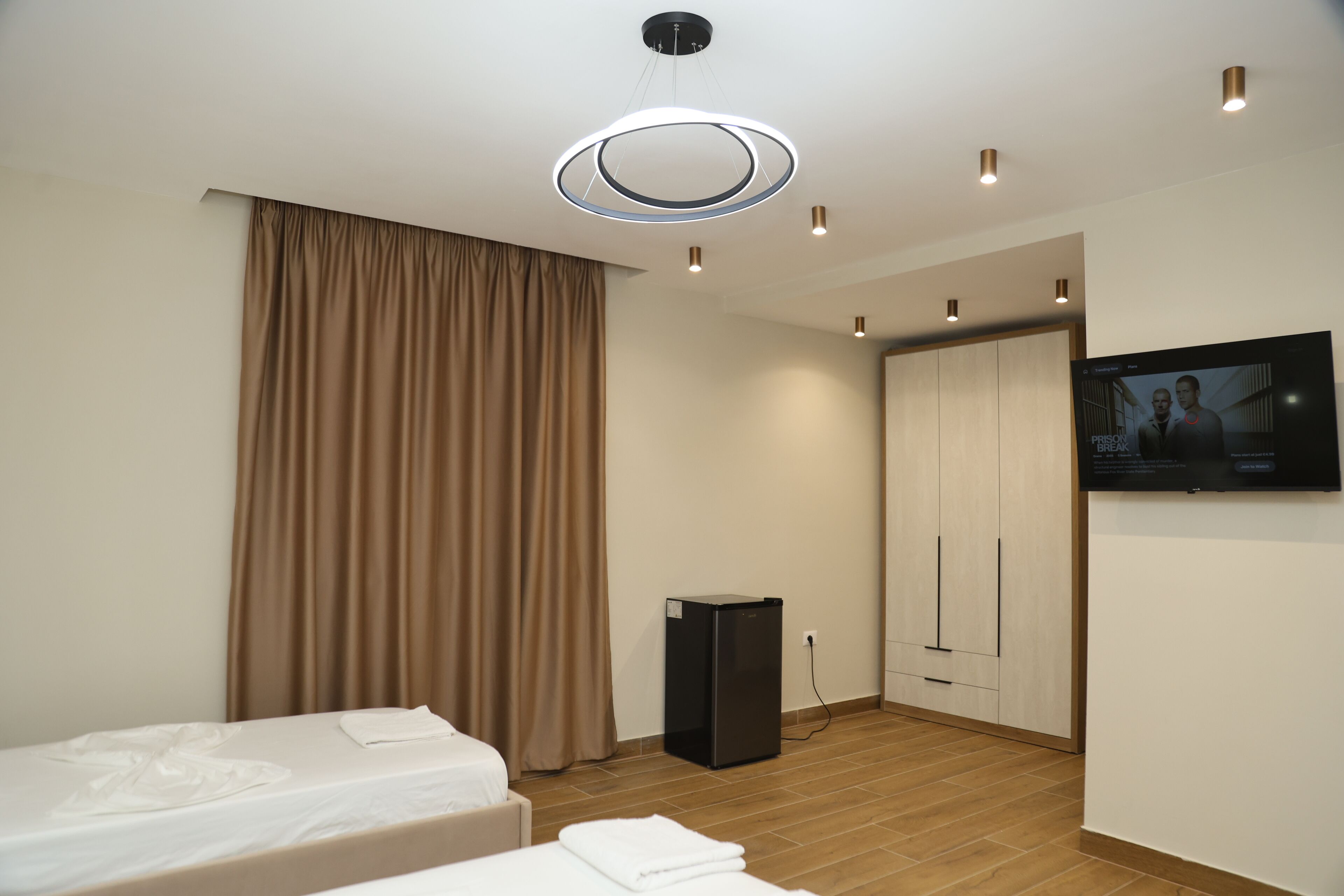 Ein modernes Hotelzimmer mit zwei Betten, einem Flachbildfernseher, einem Kleiderschrank und einem kleinen schwarzen Lautsprecher.