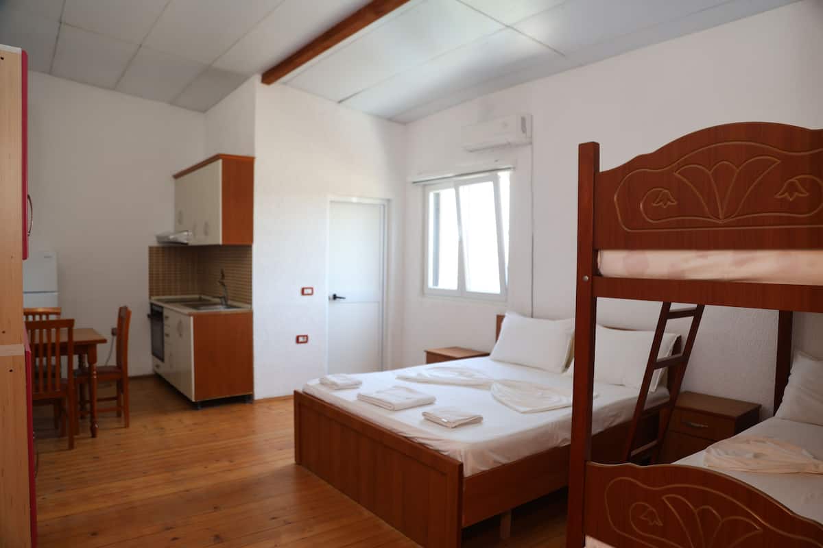 Una habitación con literas de madera, una pequeña cocina americana, un comedor y un ventanal.