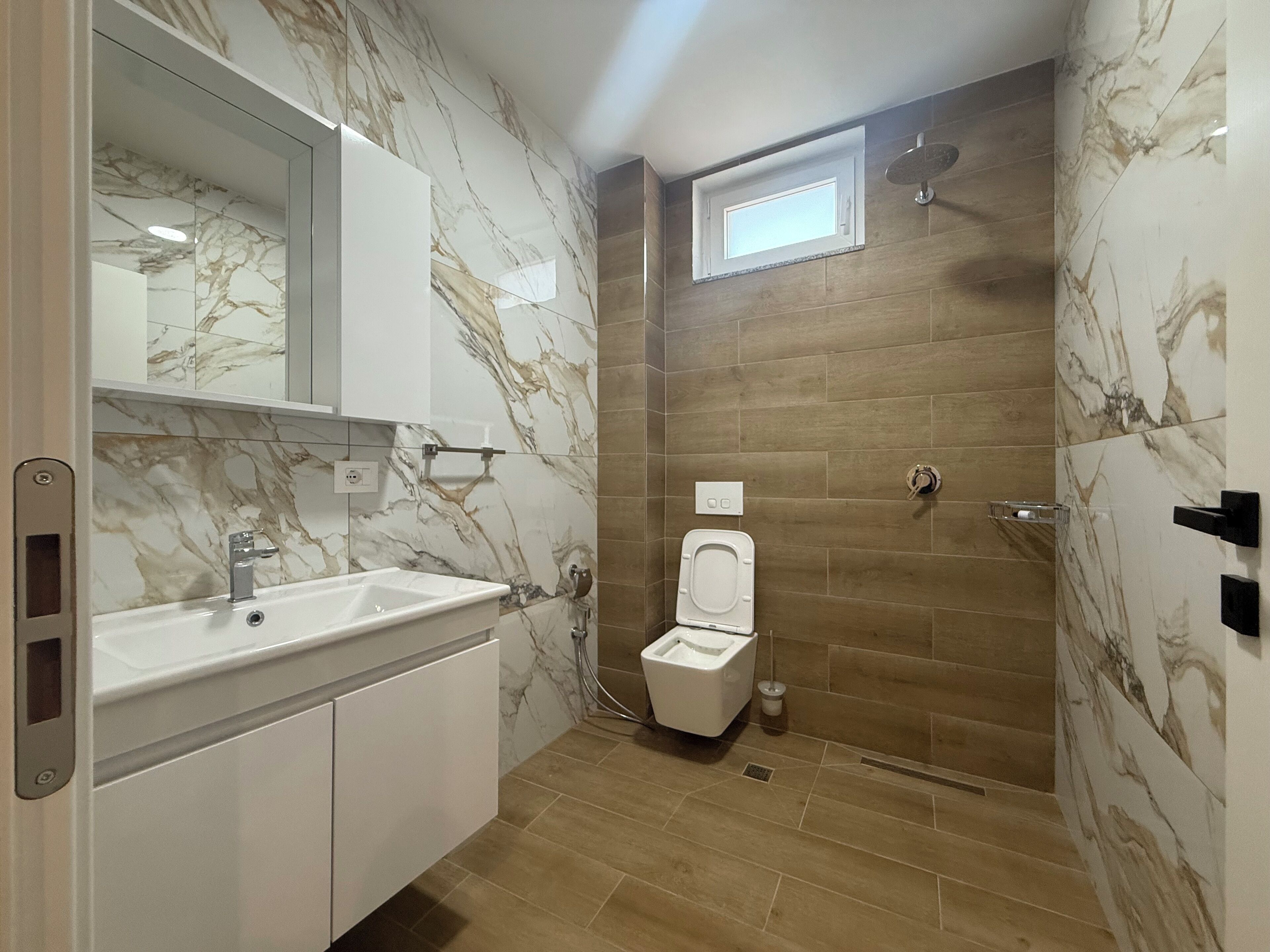 A modern bathroom with a marble vanity, a toilet, and a shower area.