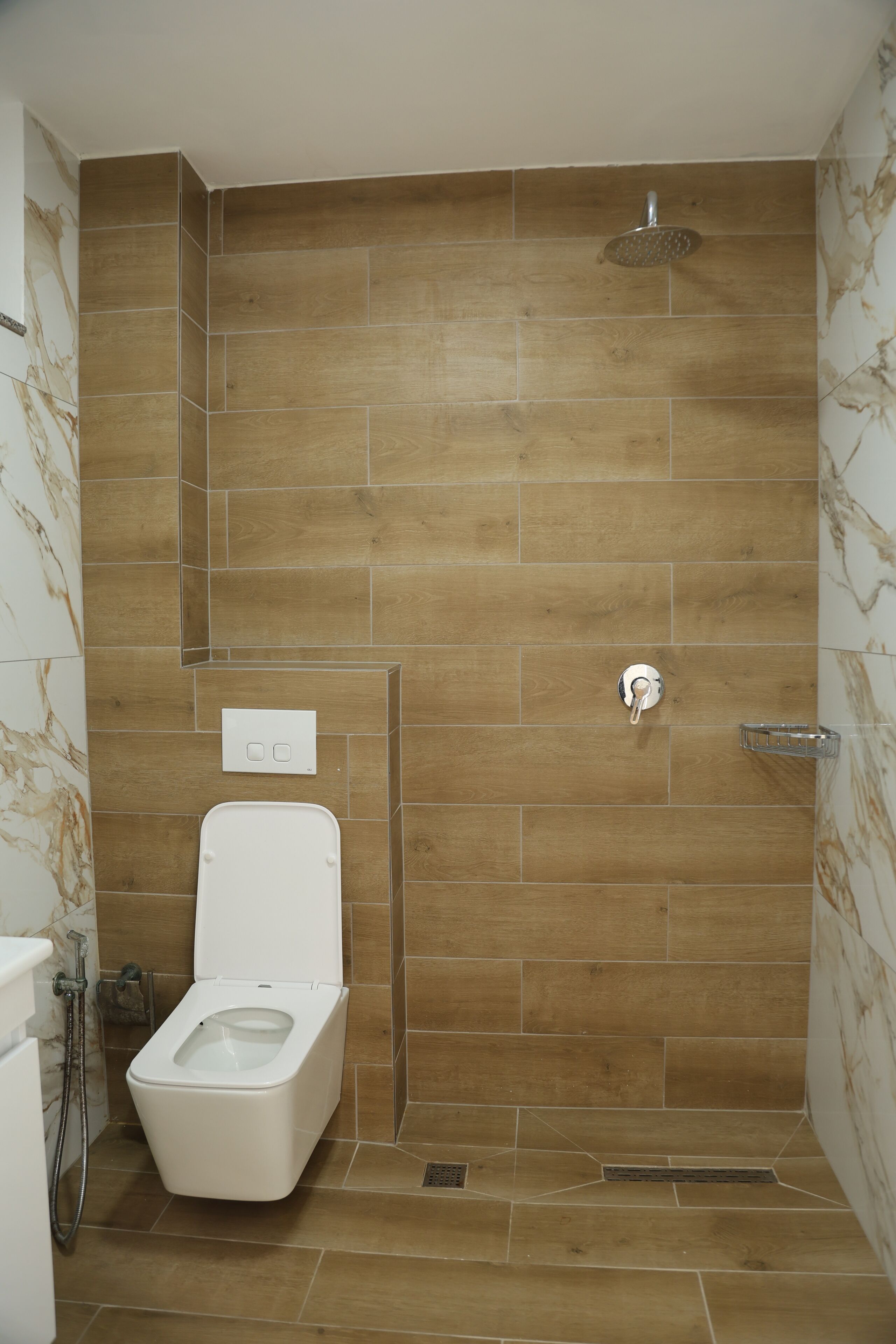 A bathroom with a wooden-tiled shower wall, a toilet, and a showerhead.