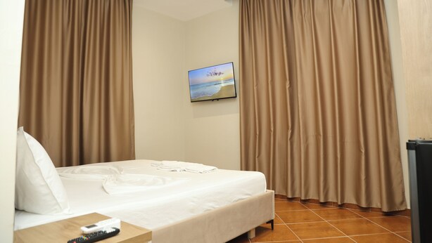 A hotel room with a bed, curtains, a remote control, a picture on the wall, and a trash bin. - Kalpazo Hotel Tommy Durres (Katundi i Ri)