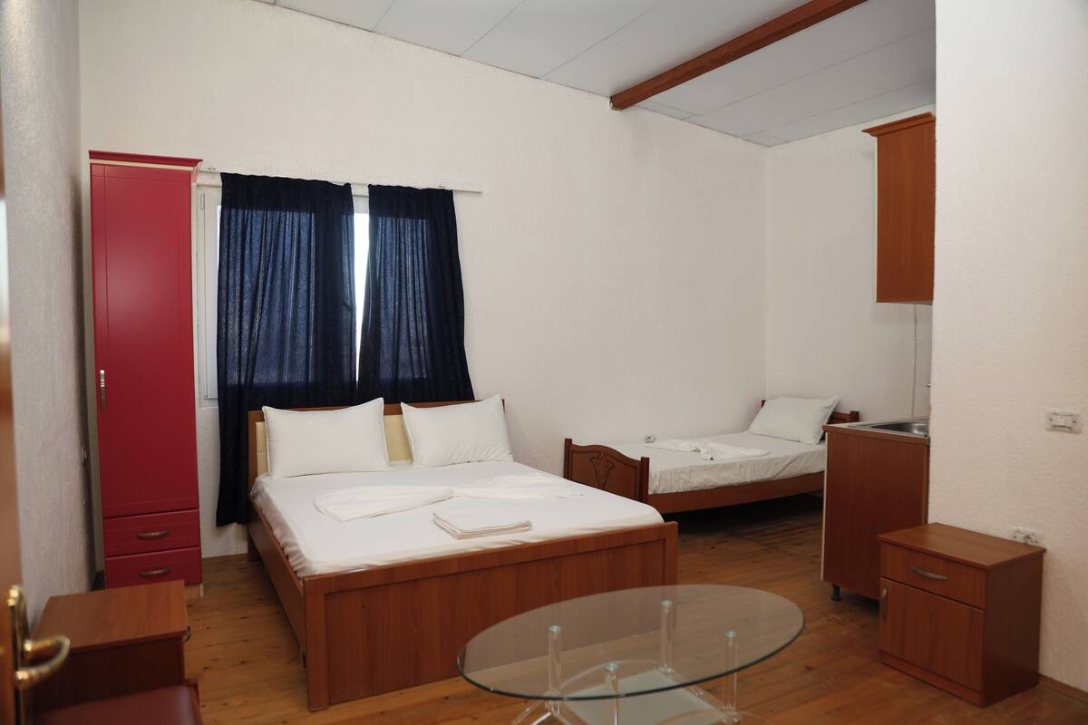 Una habitación con dos camas, un armario rojo, una mesita y un espejo.