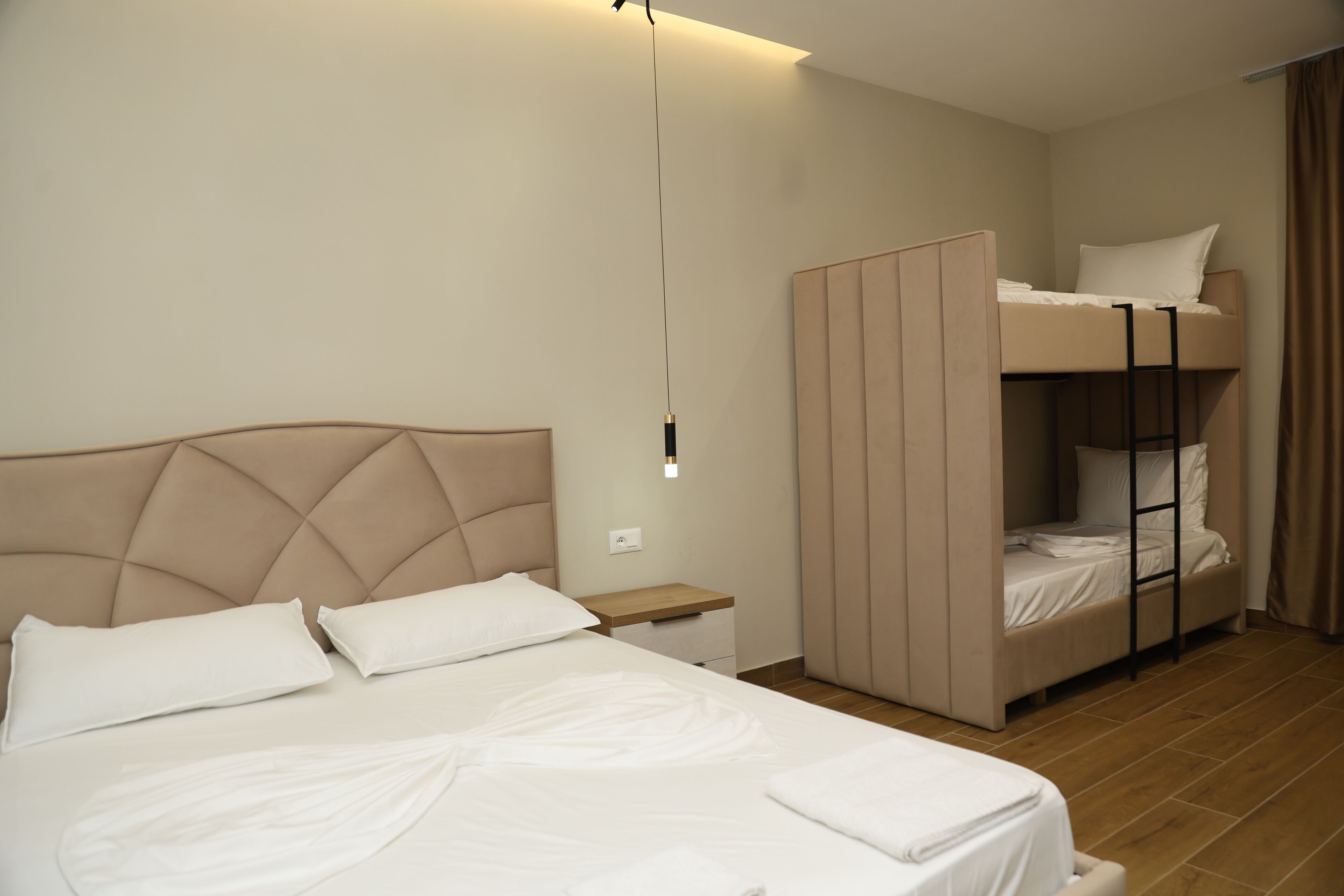 A hotel room with a large bed, a bunk bed, a bedside table, and a hanging light fixture.