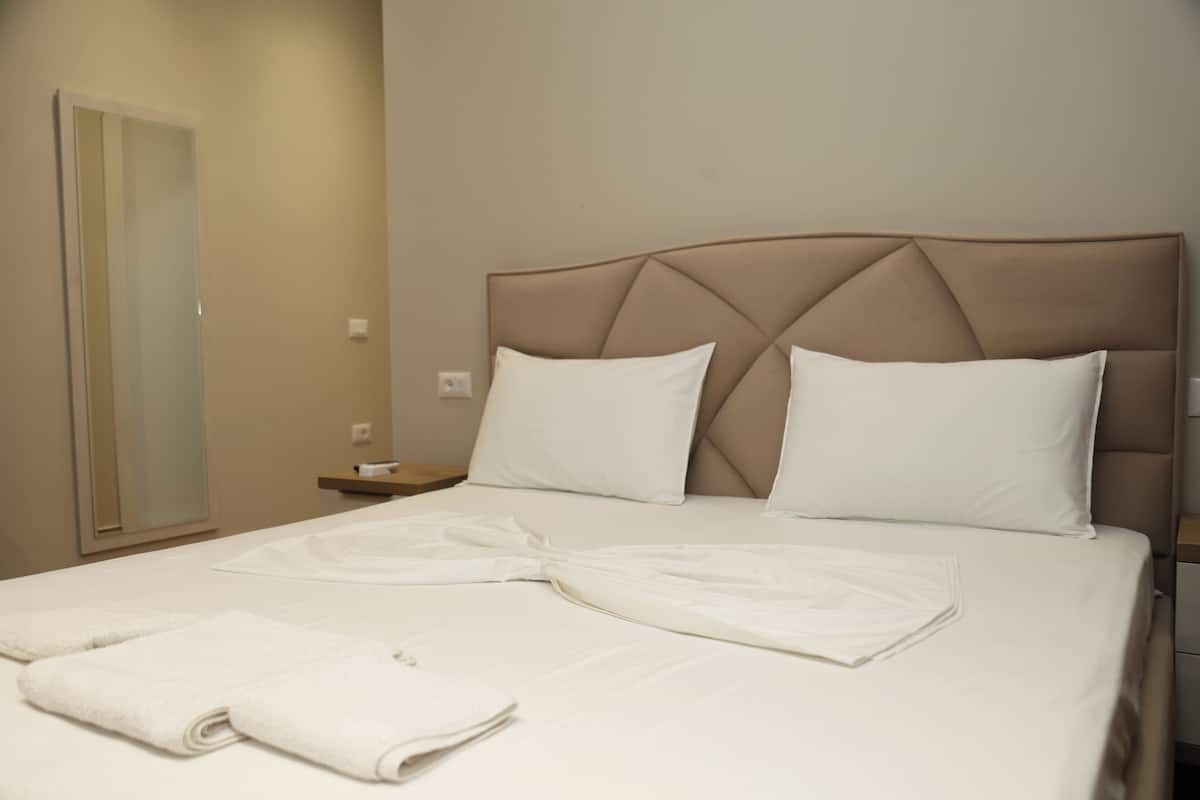 Una cama bien hecha con dos almohadas, una mesita de noche y un espejo.