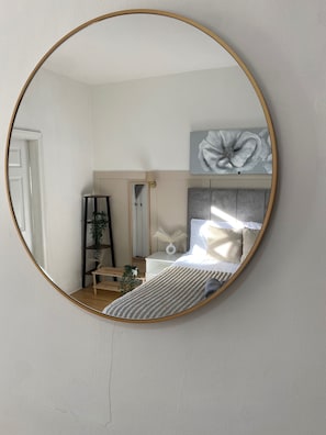 A bedroom with a round mirror, a bed with a headboard, a bedside table, a plant, and a wall-mounted artwork.