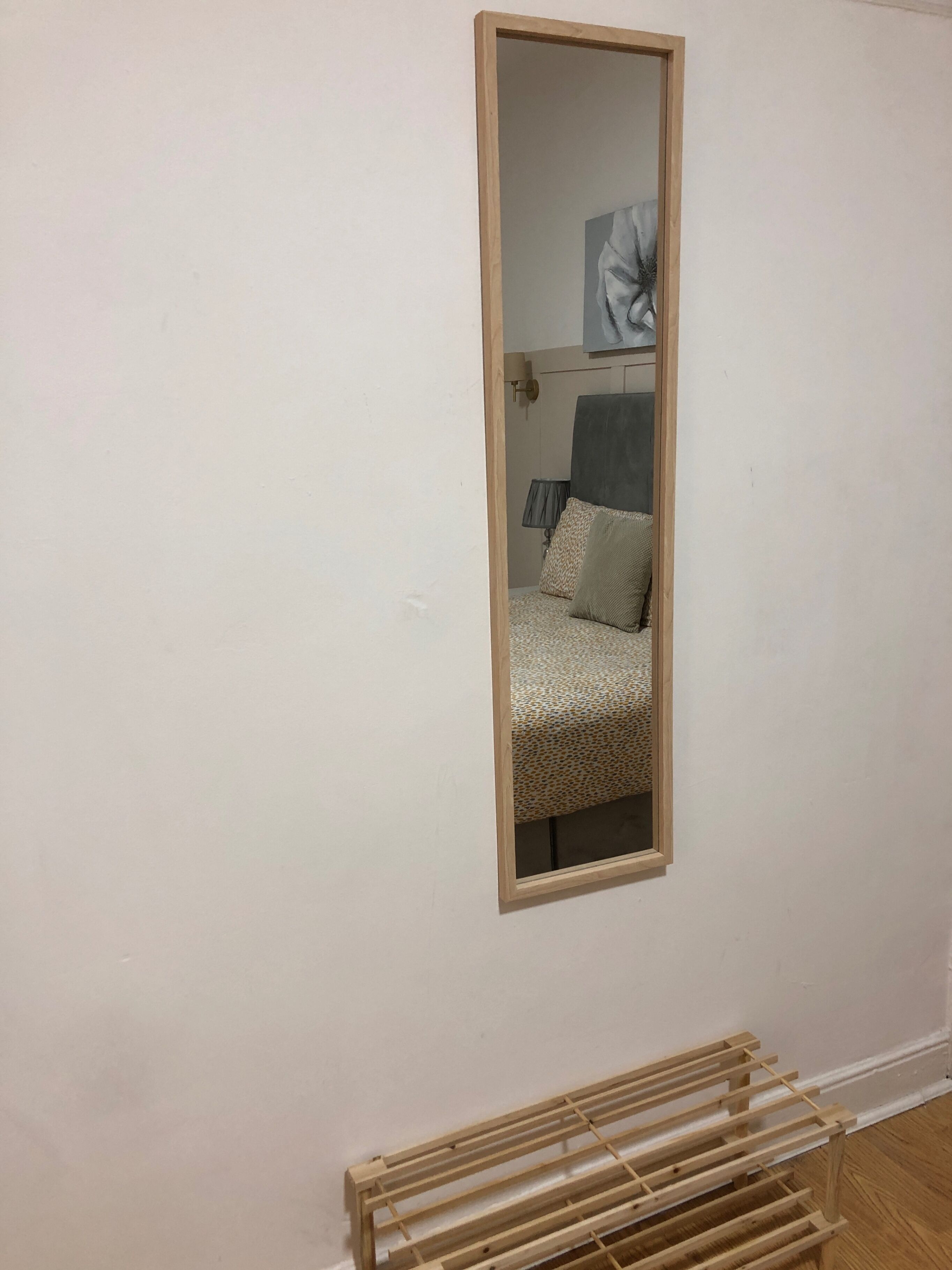 Ein Zimmer mit einem großen Spiegel an der Wand, einem Bett mit gemusterten Textilien und einem hölzernen Wäscheständer.