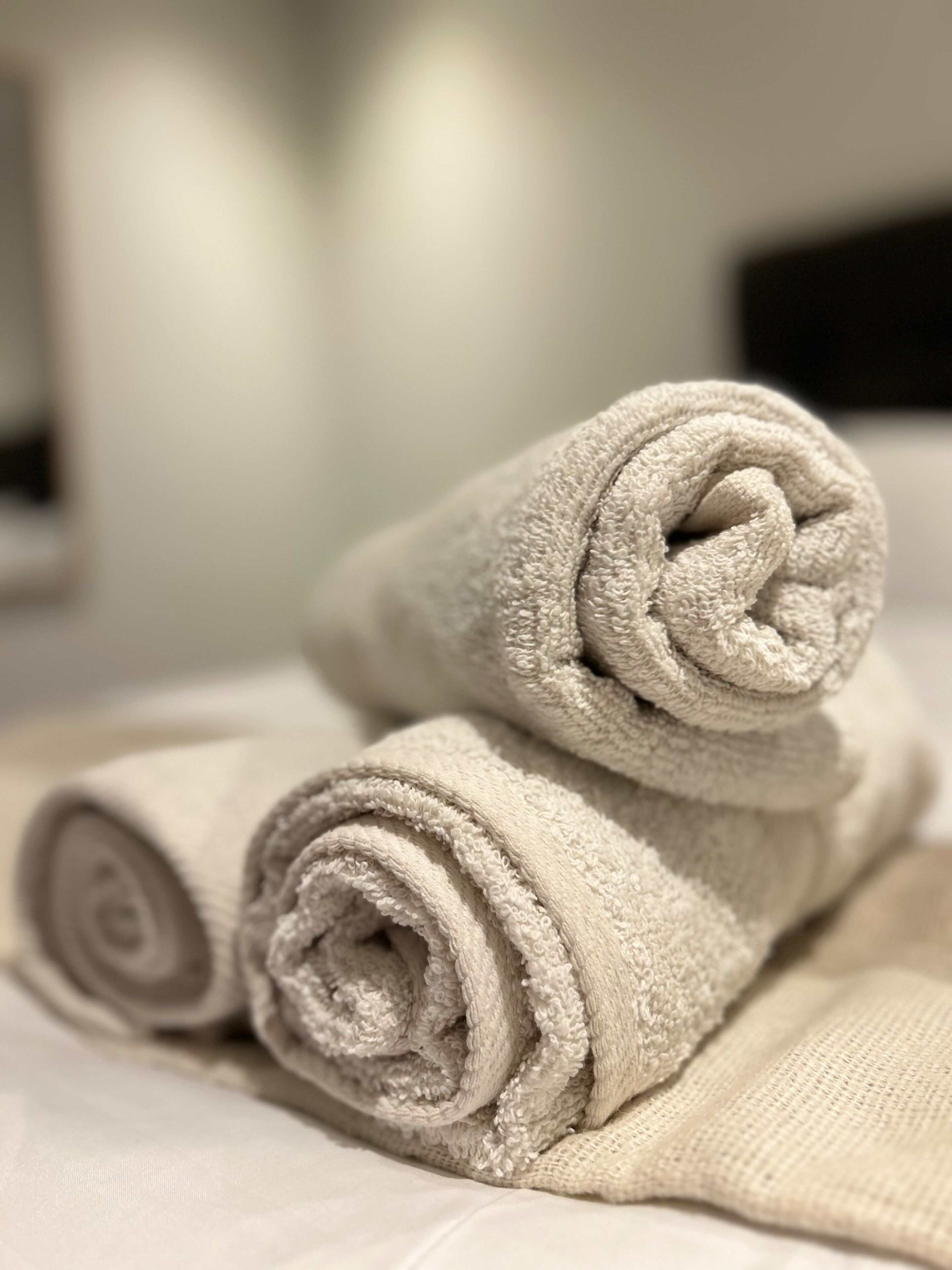 A neatly folded beige towel on a bed with a white bedspread.