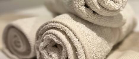 A neatly folded beige towel on a bed with a white bedspread.