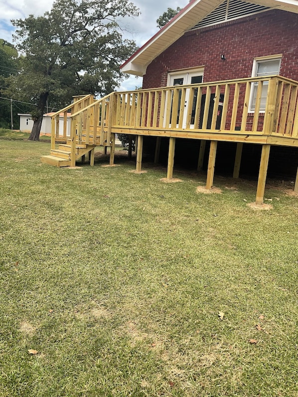 A wooden deck with a staircase leading to a covered area, adjacent to a brick building.