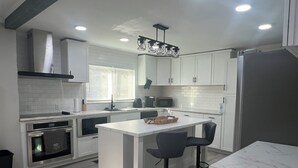 Una cocina moderna con armarios blancos, una isla central con taburetes de bar, un horno empotrado y una campana extractora de acero inoxidable.